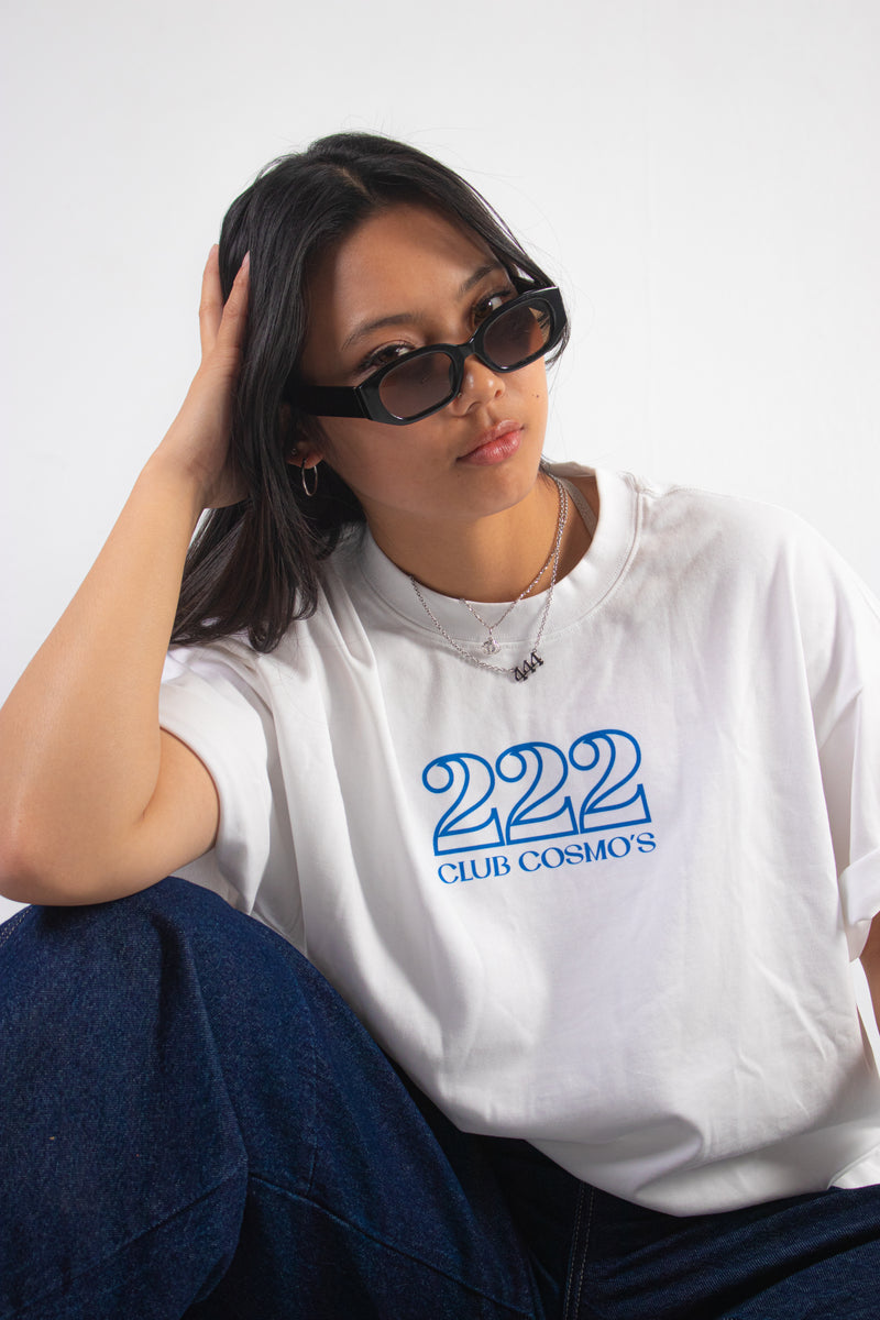 Model wearing shades and a white t-shirt with '222 Club Cosmo's' text, sitting against a plain background.