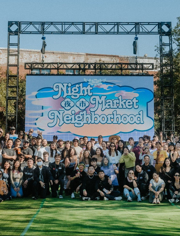 Group of people posing in front of a 'Night Market Neighborhood' sign at an outdoor event.