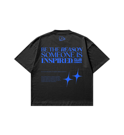 A black short-sleeve t-shirt shown from the back, featuring a large blue graphic print with the text 'BE THE REASON SOMEONE IS INSPIRED' and 'CLUB COSMOS' near the upper back.
