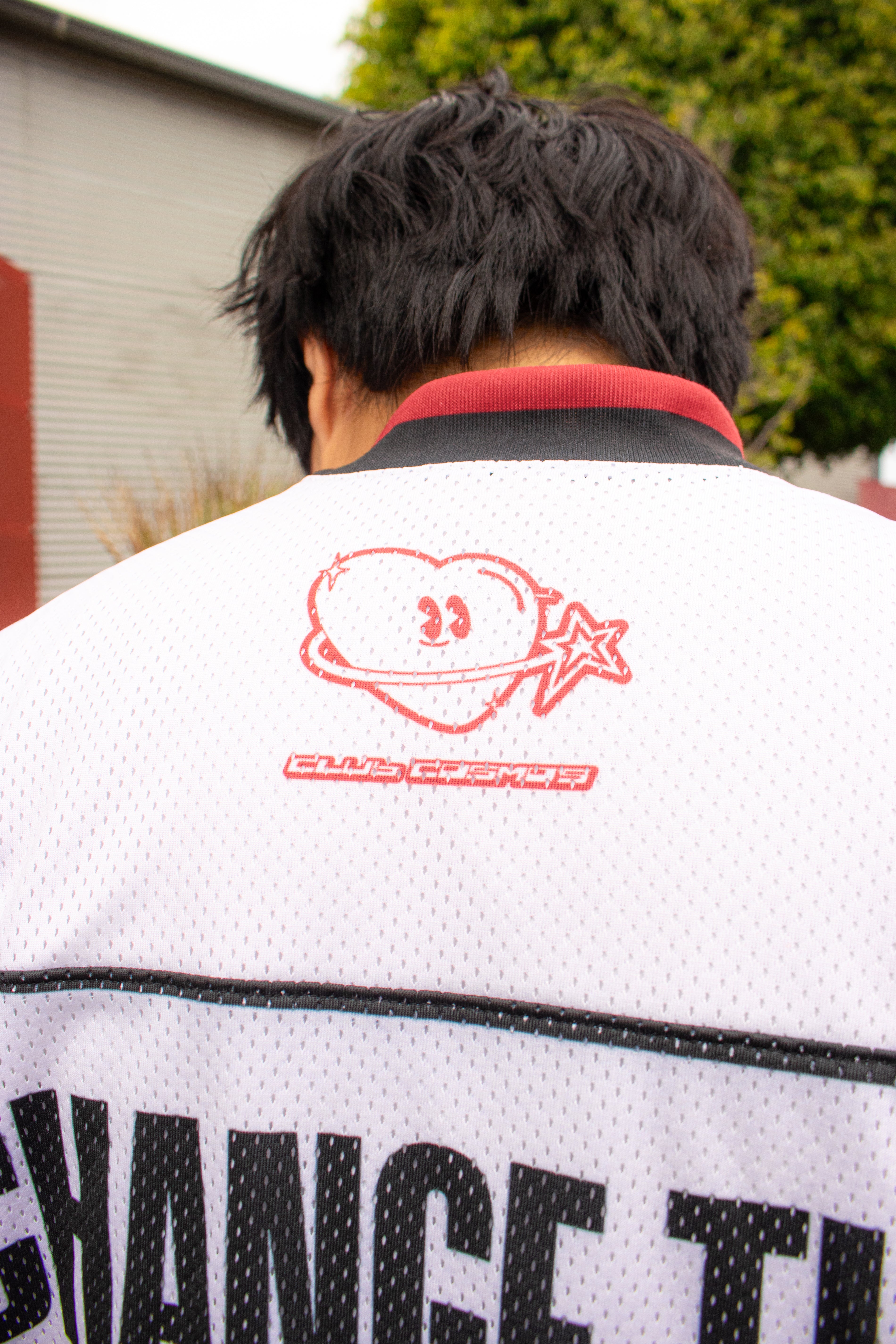 Model showcasing the back of a white sports jersey with 'Club Cosmo's' branding.