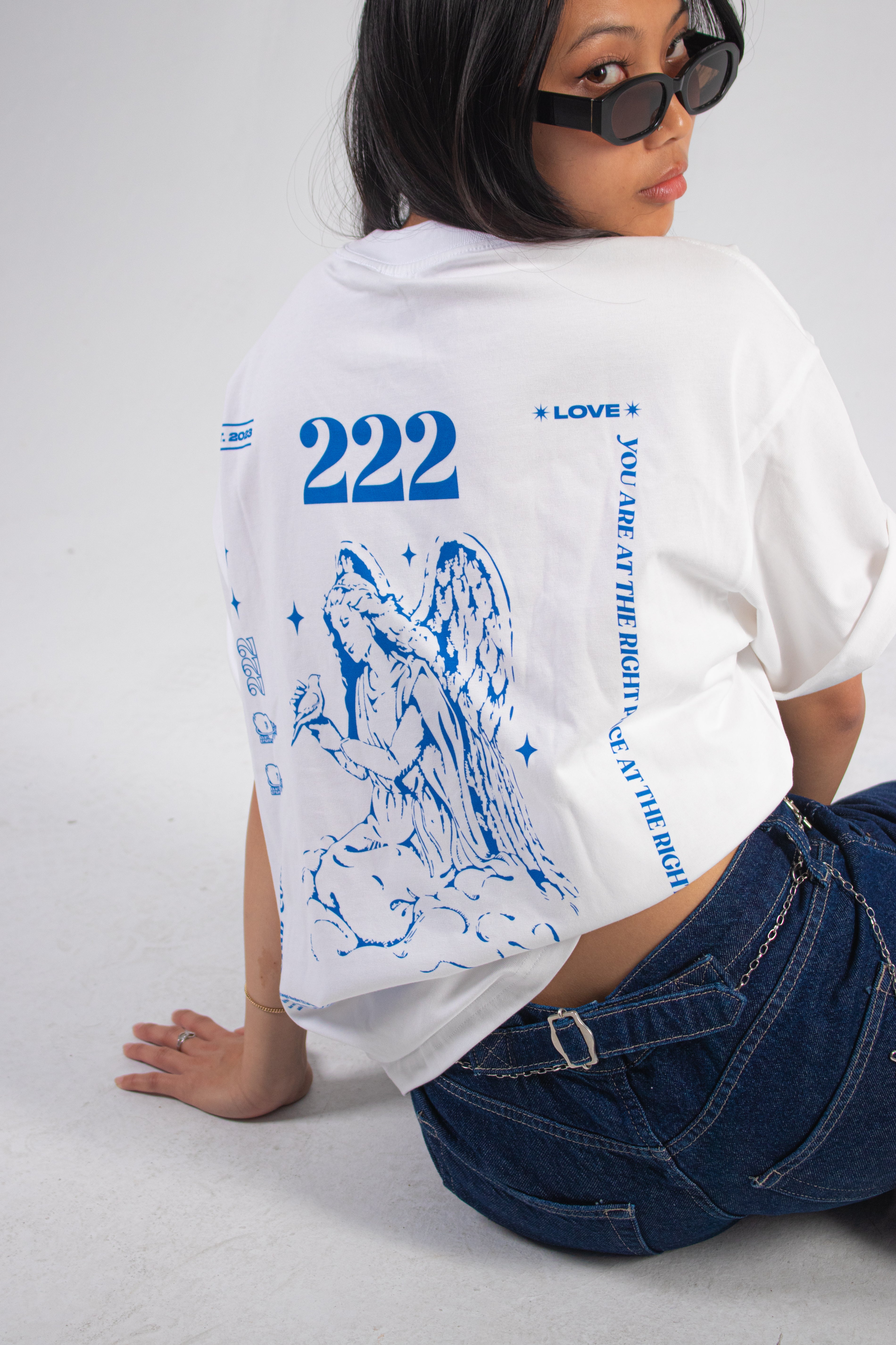 Model wearing shades and a white t-shirt with blue Club Cosmo's angel number graphics and text on a plain white background.