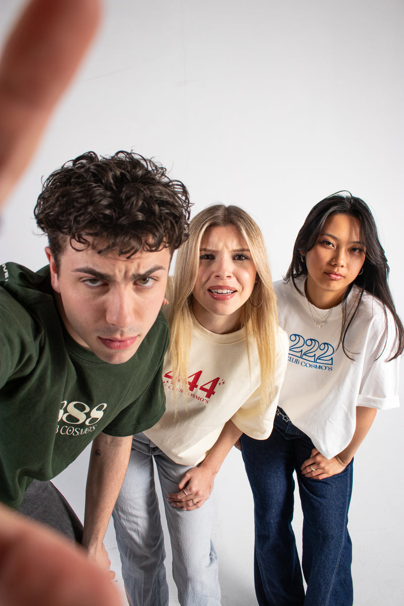 Three models wearing Club Cosmo's angel number branded t-shirts against a white background.