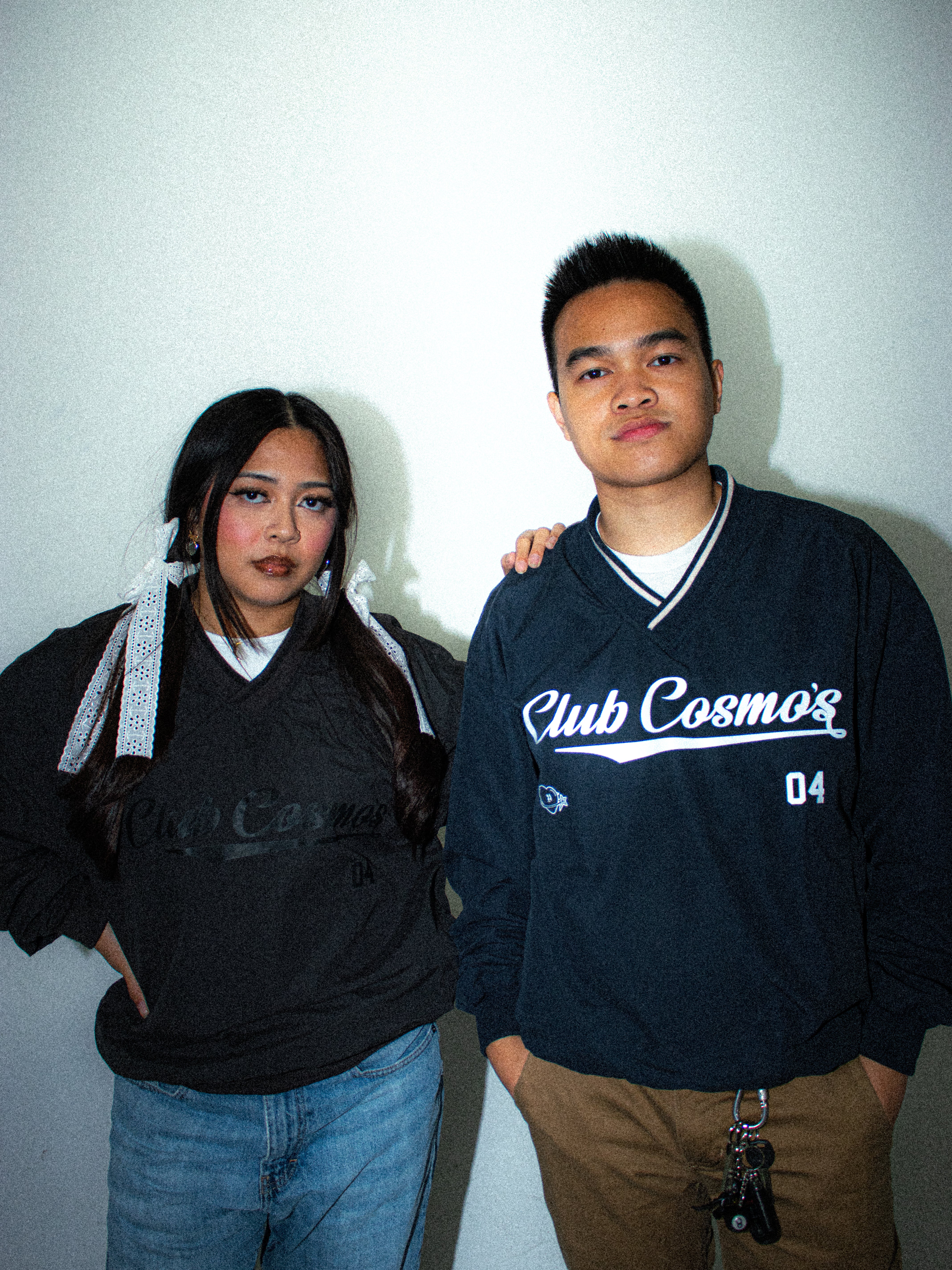 Two people standing side by side wearing a Club Cosmo's windshirt against a plain background.