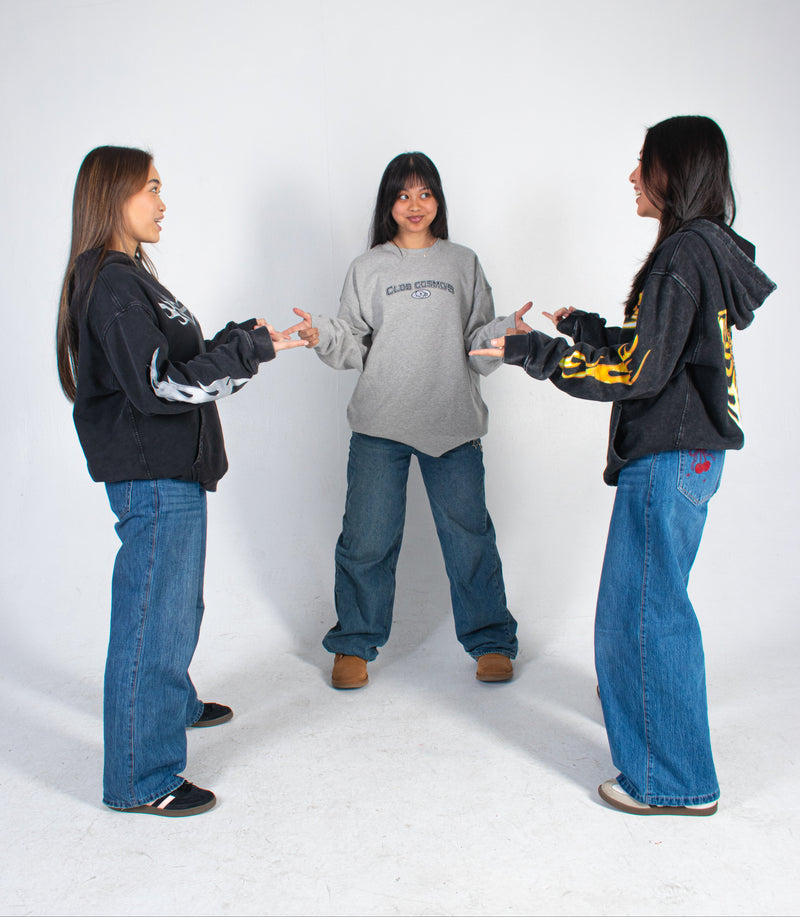Three models standing in a circle, facing and pointing at each other wearing Club Cosmo's merchandise on a white background.