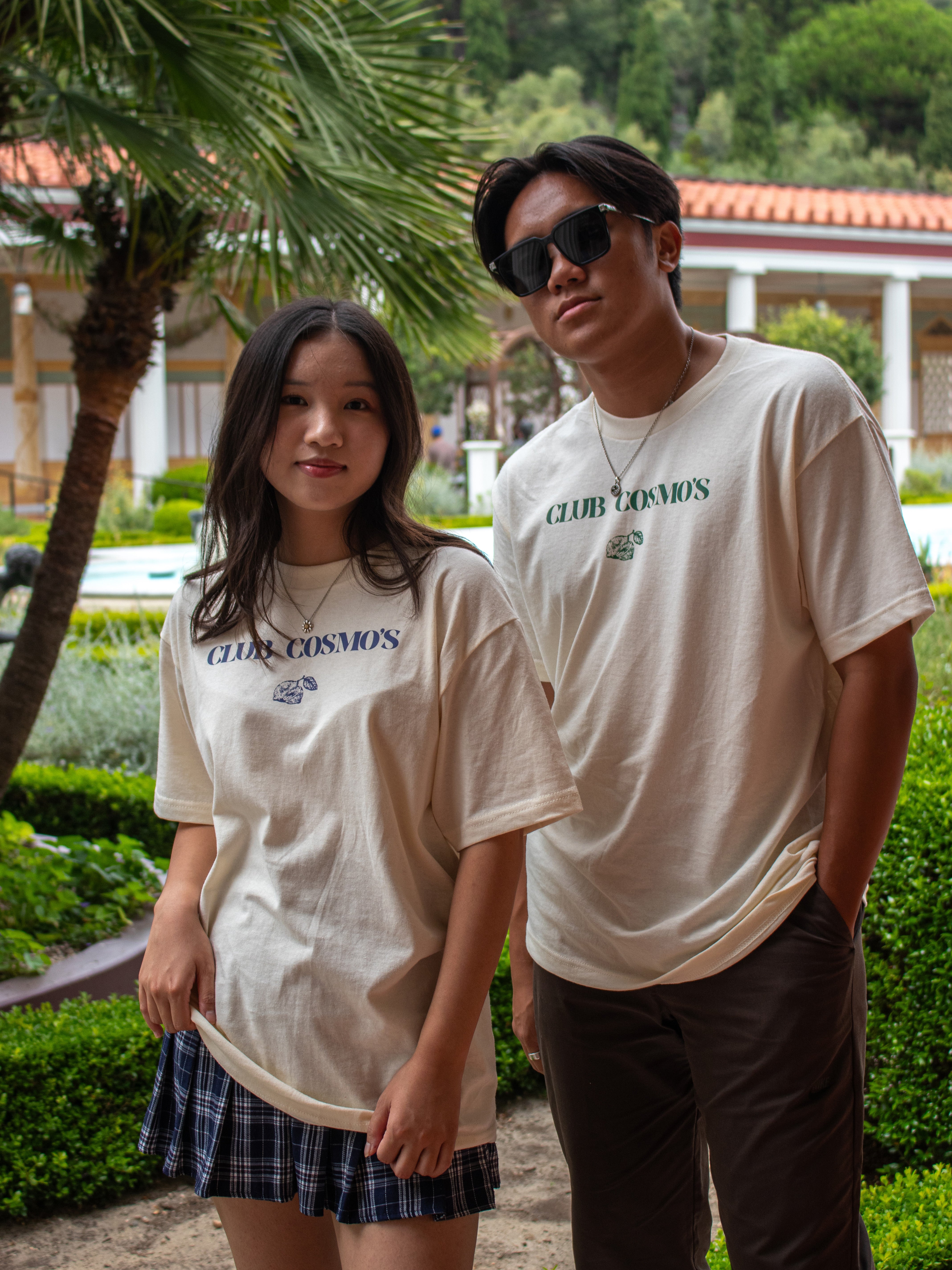 Two models wearing matching 'Club Cosmo's' lemonade tees outdoors with greenery in the background.