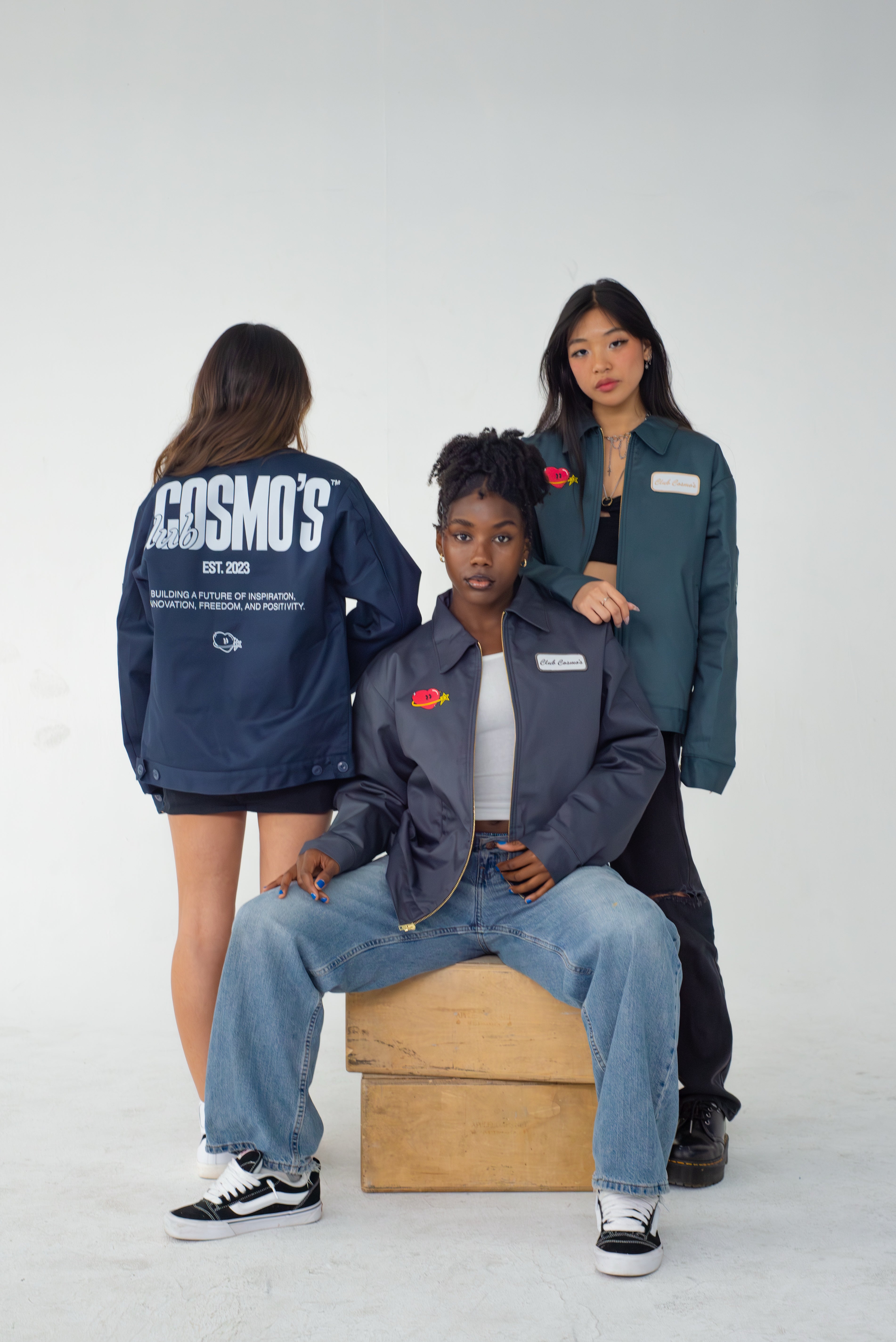 Three people wearing blue, grey, and green Club Cosmo's utility jackets on a white background.