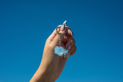 Hand holding a Club Cosmo's mascot keychain with a blue sky background.