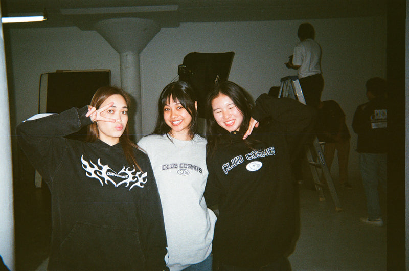 Three models wearing Club Cosmo's apparel with visible branding in an indoor studio setting.