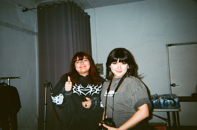 Two female Club Cosmo's team members smiling standing in a studio room with gray walls and a curtain.