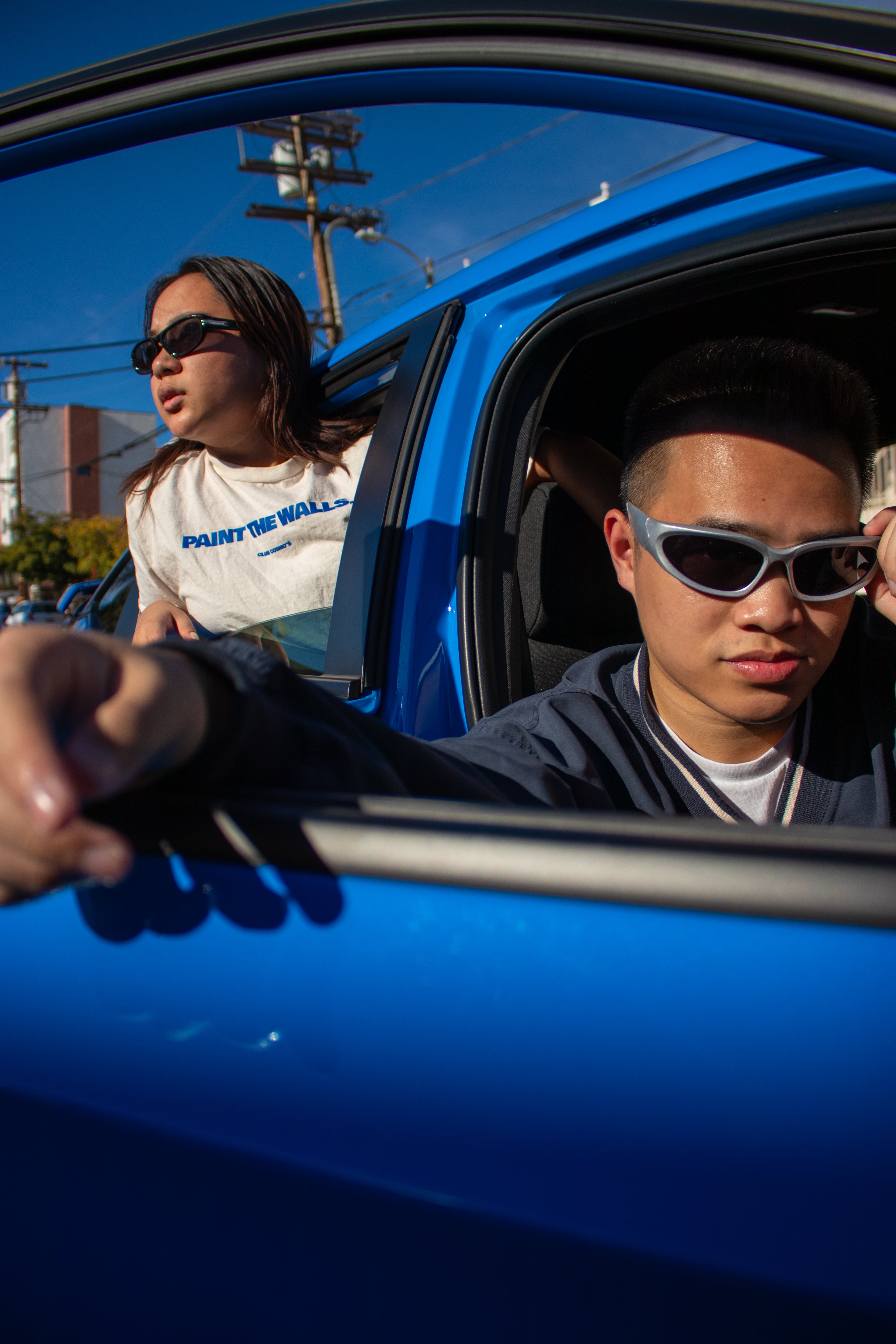 Two people in club cosmos merchandise in a blue car with one person holding onto the car door window.
