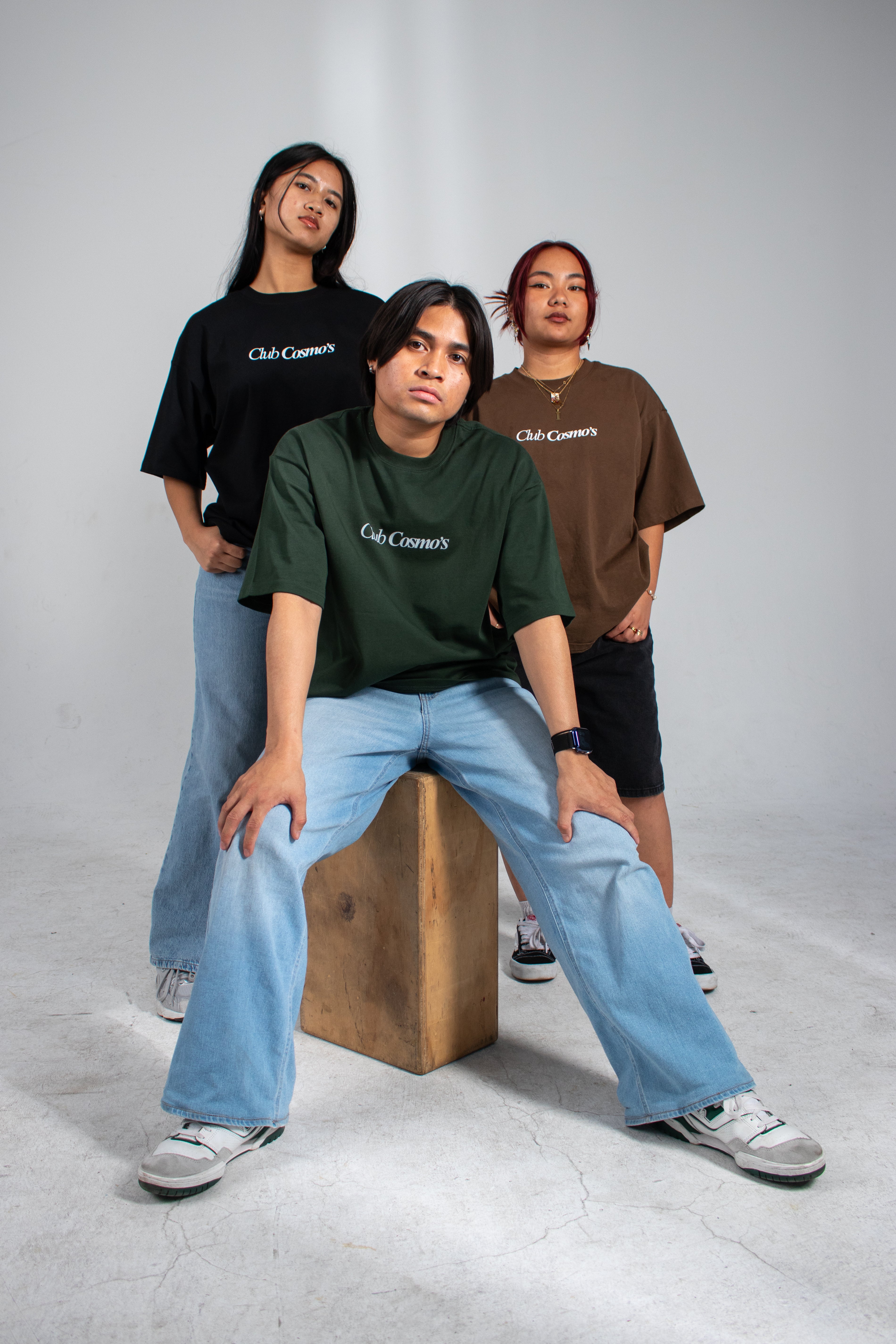 Three people wearing Club Cosmo's t-shirts on a white background.