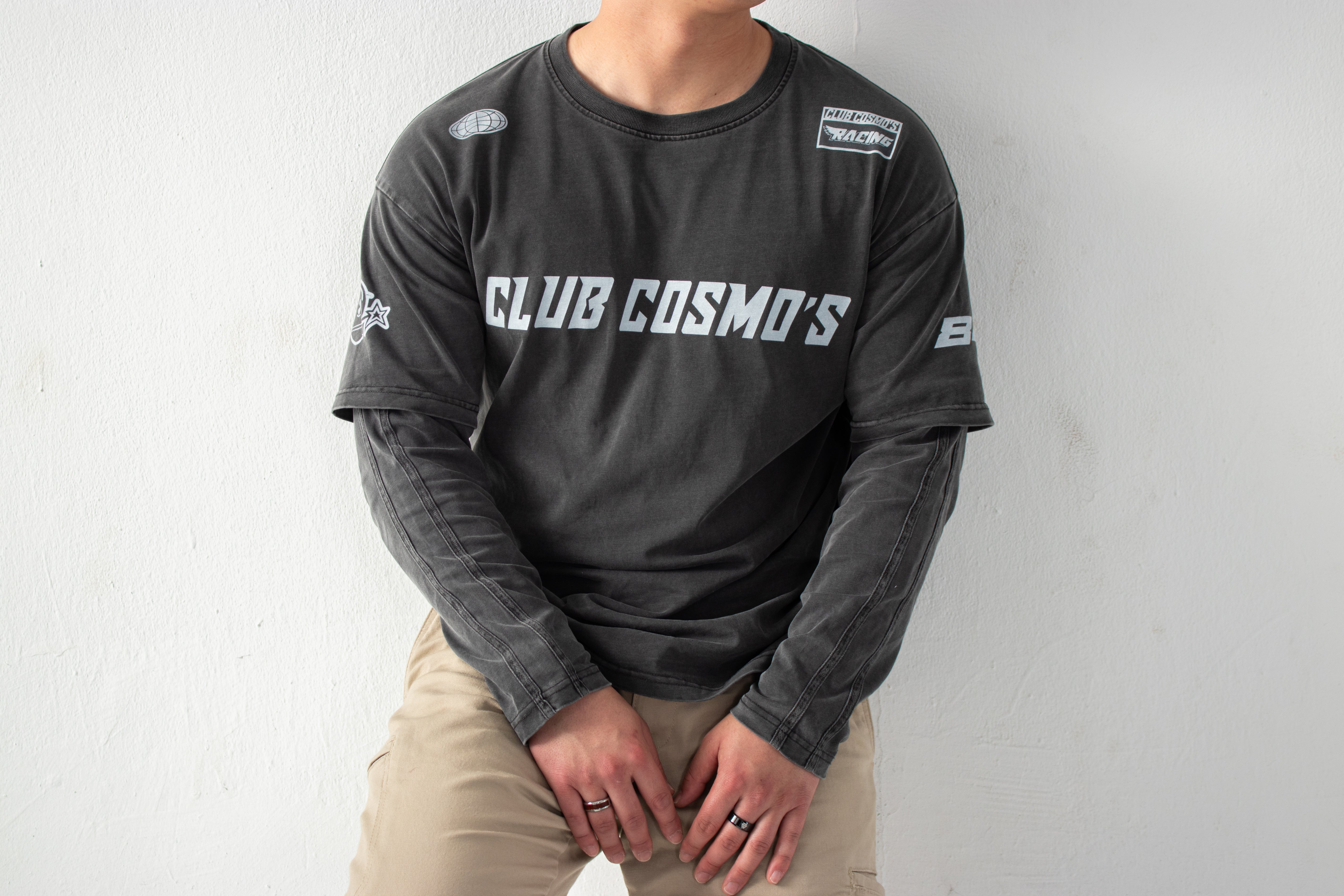 Model wearing a black long-sleeve shirt with 'CLUB COSMO'S' text and graphics on a white background.