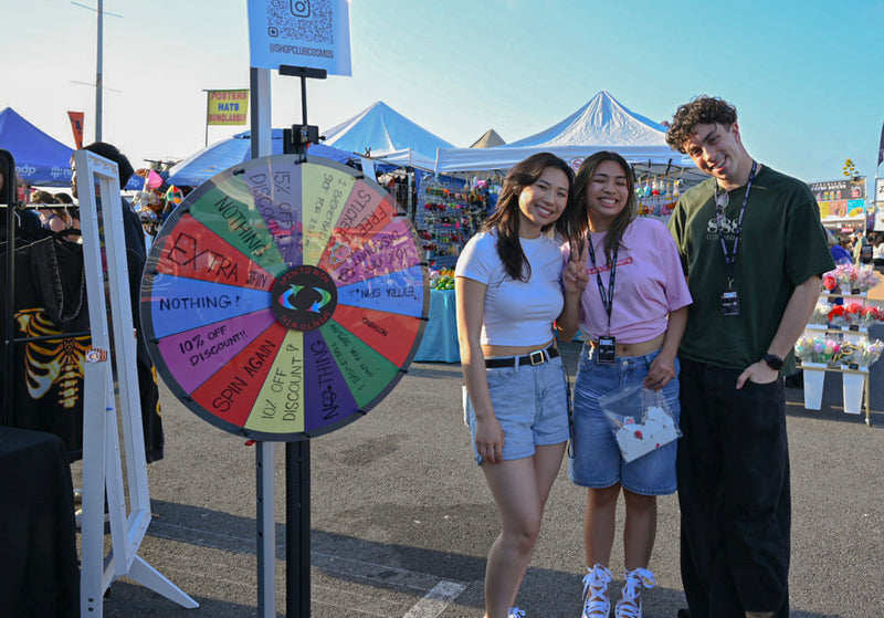 Three Club Cosmo's collectives standing next to a colorful wheel a 626 night market event.