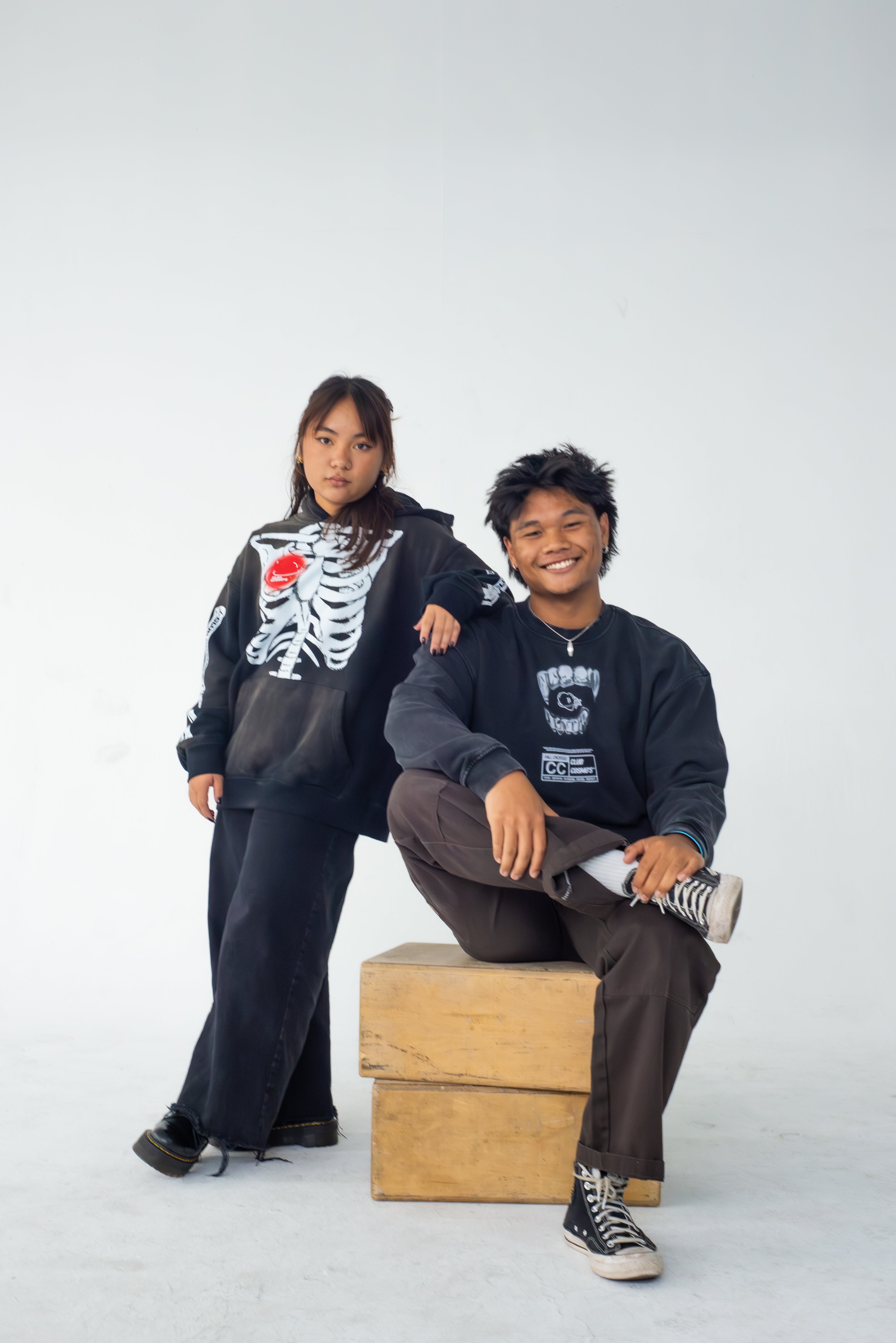 Two people wearing halloween Club Cosmo's merchandise with graphic designs on a white background.