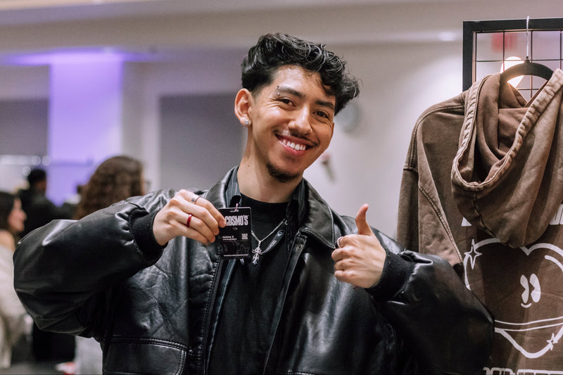 Team member in a leather jacket holding a Club Cosmo's Collective card with a blurred indoor background.