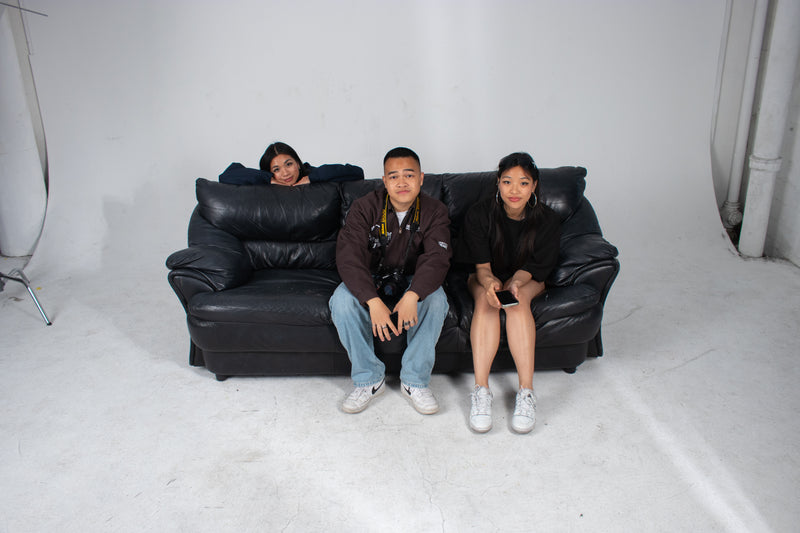 Three Club Cosmo's team members sitting on a black leather couch against a white background.