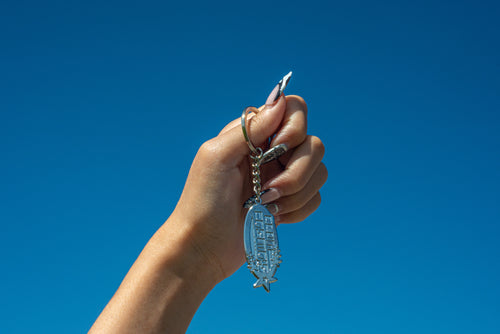 Hand holding a Club Cosmo's star logo keychain against a clear blue sky.