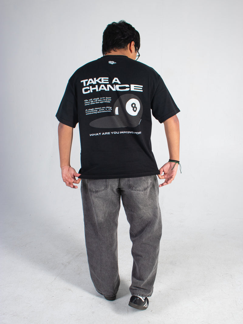 Model wearing a black tee with inspirational text and an eight ball graphic on the back, standing against a plain background.