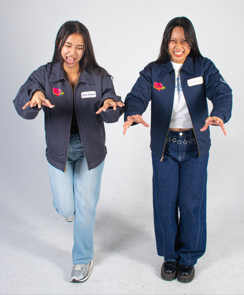 Two models making funny faces wearing matching Club Cosmo's utility jackets with visible branding on a white background.