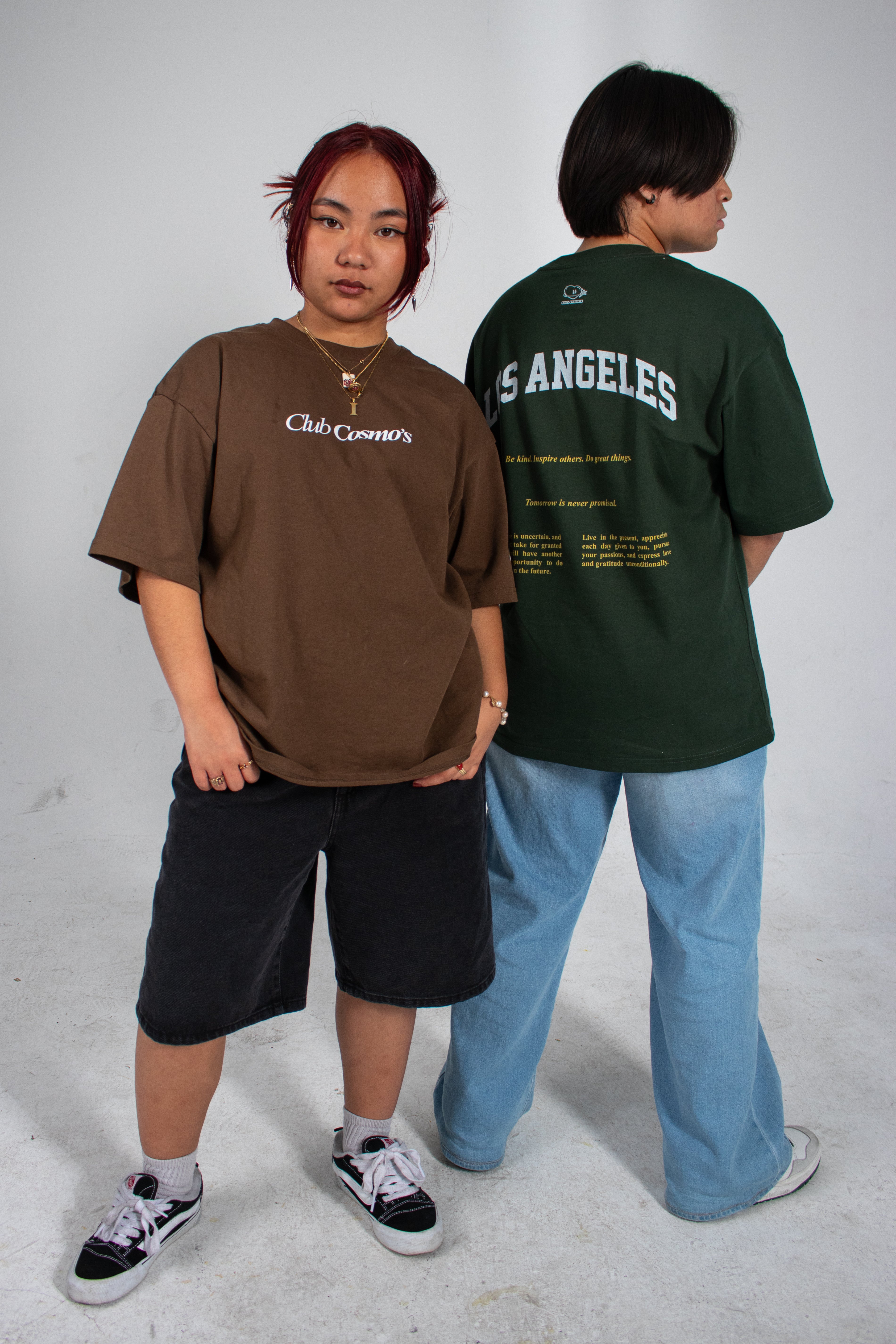 Two people wearing earth tone t-shirts with text 'Club Cosmo's', standing against a plain white background.