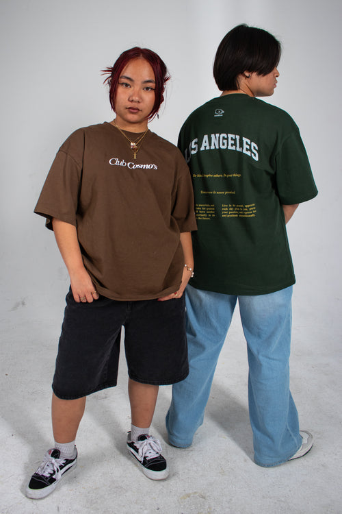 Two people wearing earth tone t-shirts with text 'Club Cosmo's', standing against a plain white background.