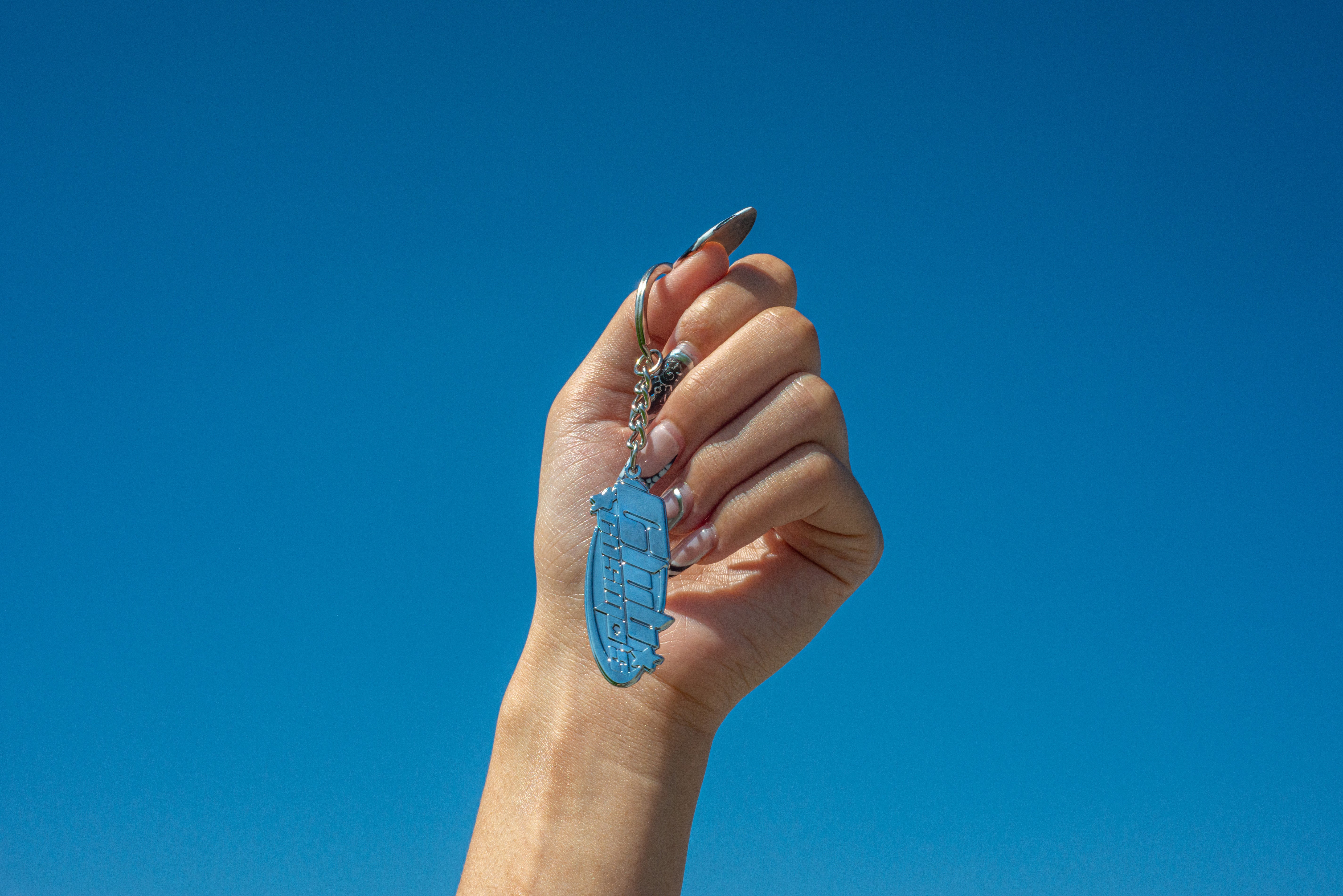 Hand holding a chrome plated Club Cosmo's keychain against a clear blue sky.