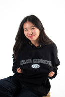 Model sitting down wearing a black hoodie with 'Club Cosmos' text on a white background.