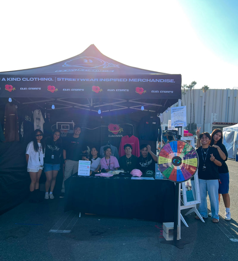 Team members outdoors standing in front of a Club Cosmo's branded booth with promotional items.