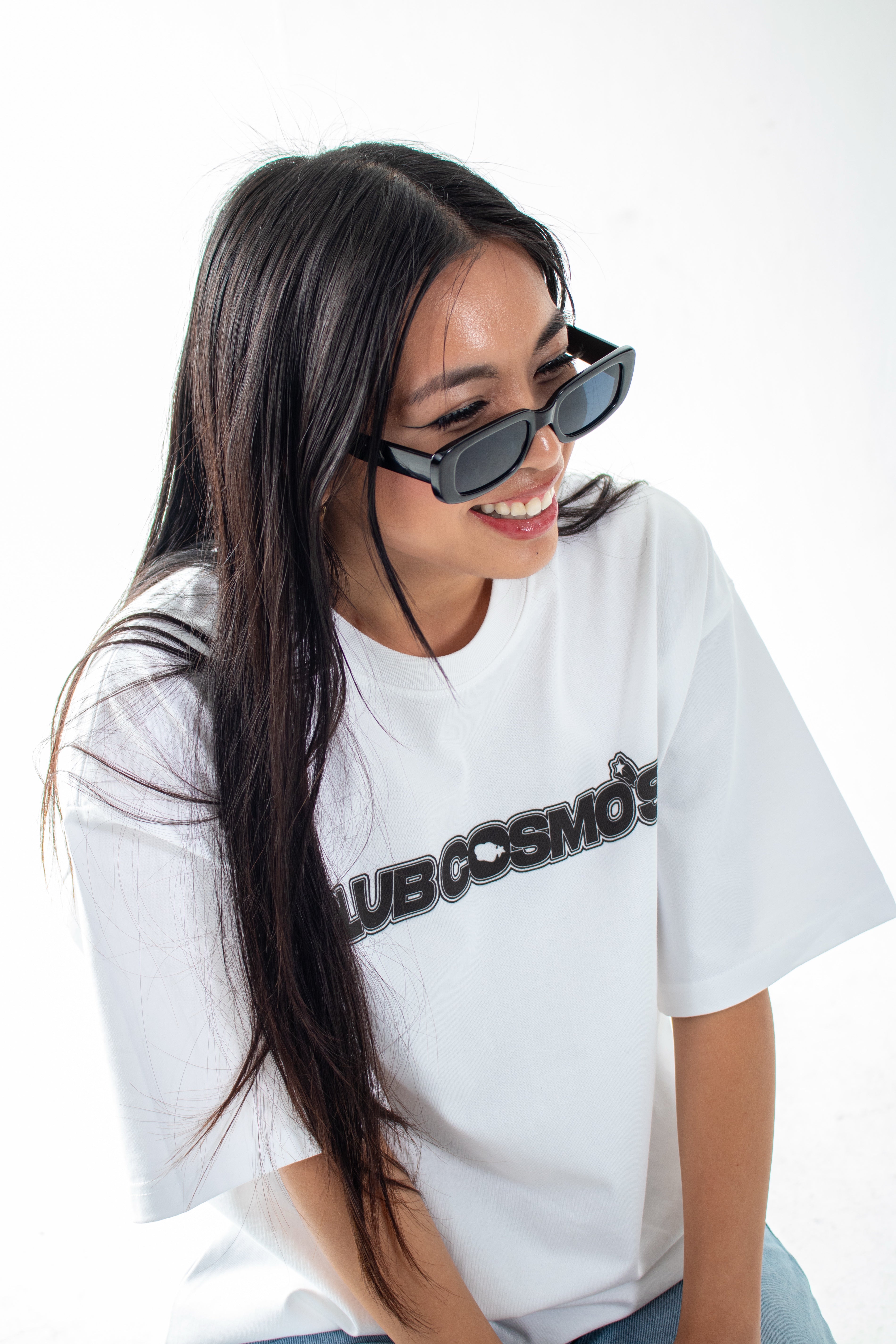 Model wearing a y2k aesthetic white t-shirt with 'Club Cosmo's' text and black sunglasses on a white background.